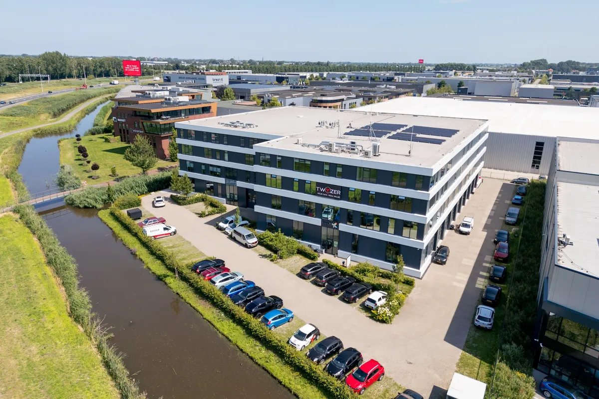 Luchtfoto van het Twyzer-kantoorpand met het bedrijfslogo op de gevel, parkeerplaats en kanaal in de omgeving